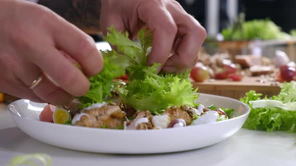 male chef in an apron decorates lettuce salad with vegetables on plate