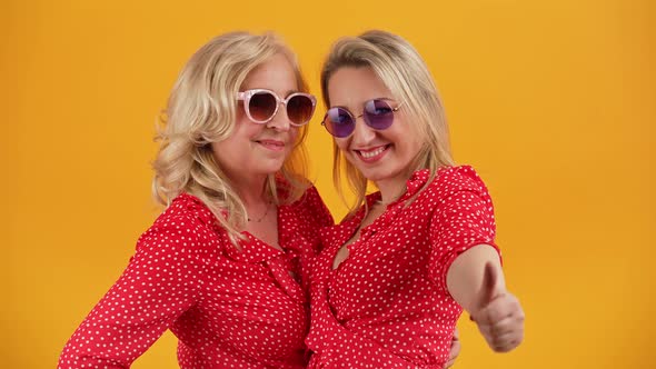 Studio Medium Shot Over Orange Background of Two Caucasian Women in Their 40s Laughing and Hugging