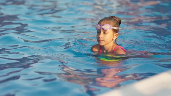 A Girl in a Bright Swimsuit with Swimming Goggles Dives Into a Pool with Clear Transparent Water