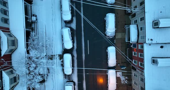 Rising aerial during snowstorm. Homes rooftops covered with snow. Cars parked in street.