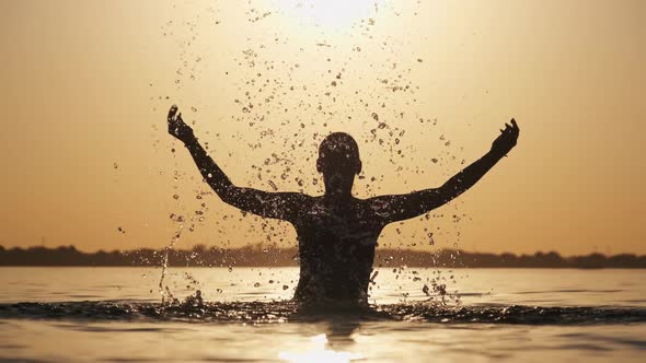 Silhouette of Young Playful Cheerful Woman Splashing River Water at Sunset