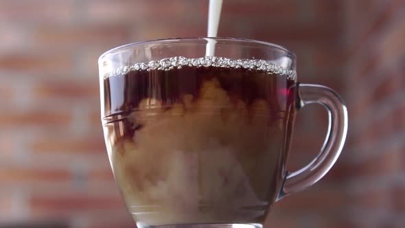 Pouring milk into hot tea in a glass cup on the background of a stone brick wall outdoors