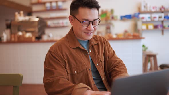 Smiling Asian young man wearing eyeglasses working on laptop