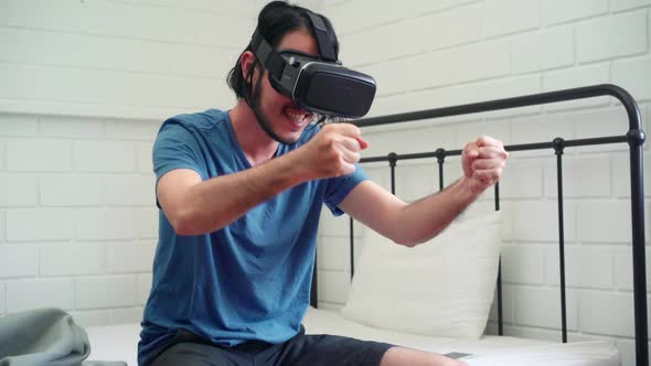 Young Asian man using glasses virtual reality simulator playing video game in bedroom