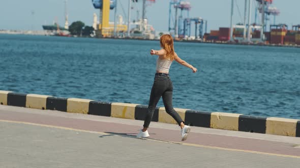 Young Stylish Funky Red Haired Woman Running Near Sea Port During Sunny Day