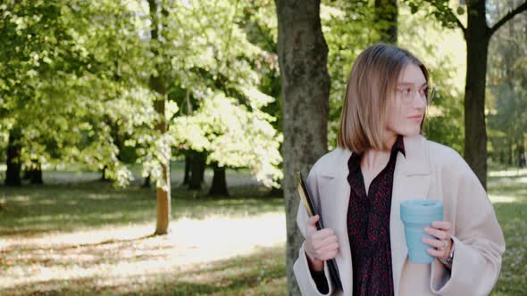 Young Girl Walks in the City Park on a Sunny Autumn Day Wearing Coat and Smiling