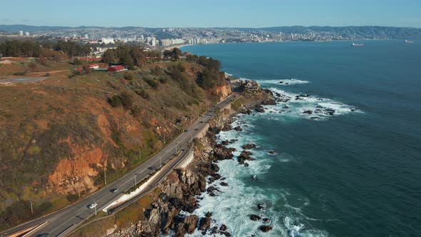 Aerial view following Avenida Borgoño waterfront coastal road alongside Reñaca affluent ocean waves