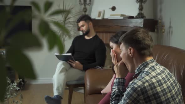 Tired Caucasian Family Sitting at the Foreground and Yawning, Psychologist Taking Notes