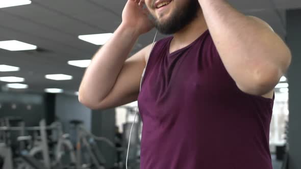 Inspired Fat Man in Headphones Walking on Gym Running Track, Endurance, Health