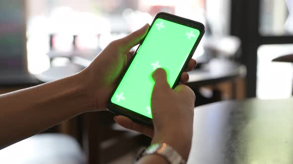 Close-Up Of Woman Hand Using Mobile Phone With Green Screen In Restaurant