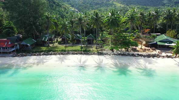 Tranquil vacations resort with beach cabins under palm trees in front of white sandy beach washed by
