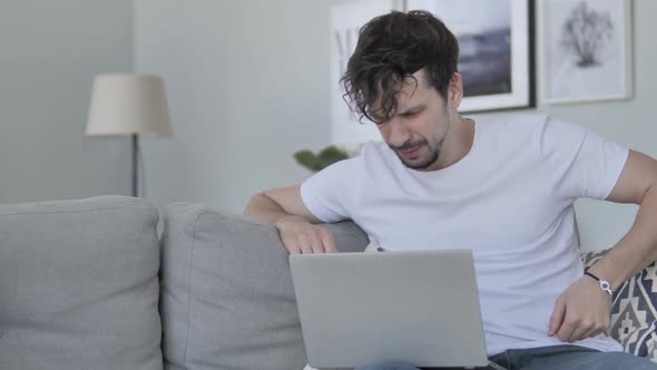 Young Man with Spinal Back Pain Sitting on Couch and Using Laptop