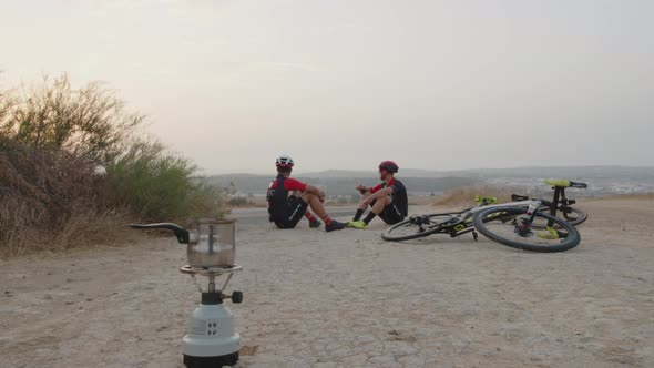 dolly shot of two professional young men bikers drinking coffe in the middle of the desert at sunris