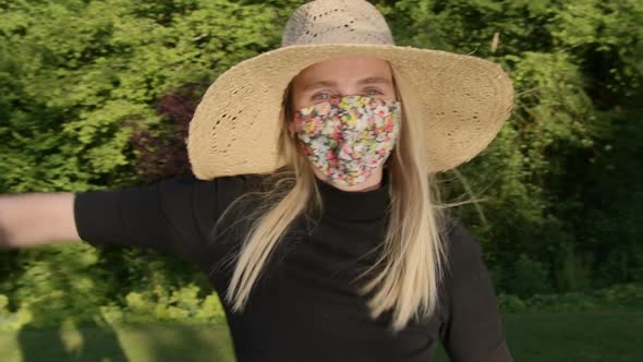 Cute woman with floral face mask making waves playfully with arms being silly on sunny day in park