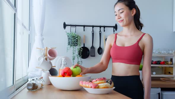 Asian sport girl in sportswear desire to chose fruit and ignore sweet donut enjoy eat healthy food.