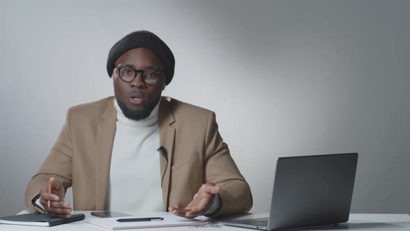 Young Afro-American Vlogger Sitting in Studio and Talking on Camera