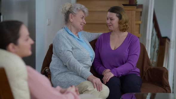 Glad Happy Senior and Adult Women Hugging Looking at Camera with Blurred Young Millennial Woman