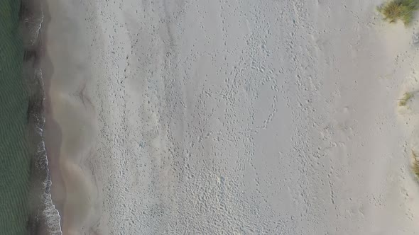 AERIAL: Top View Pan Shot of Sandy Beach with Foot Prints and Waves Crashing on a Shore