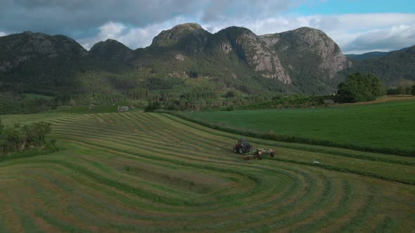 Tractor-drawn Hay Turner At Work In Green Meadow In Rogaland, Norway. wide aerial