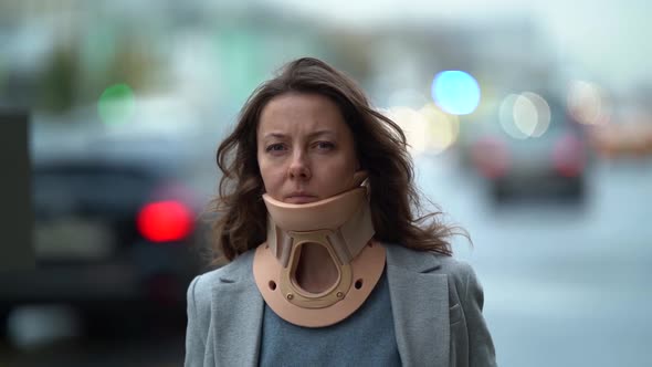 a Scowling Middleaged Woman with an Orthopedic Collar Around Her Neck Walks Down the Street Against