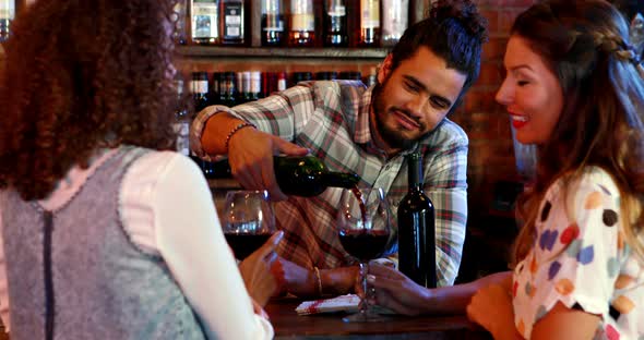 Barman serving red wine female customers at bar counter