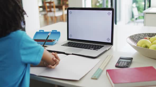 Happy biracial boy sitting at table using laptop with copy space and having online classes