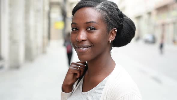 Young beautiful black woman outdoor in the city, looking at camera smiling