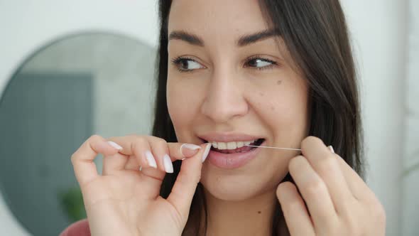 Close-up of Beautiful Woman Cleaning Teeth with Dental Floss Smiling in Modern Bathroom