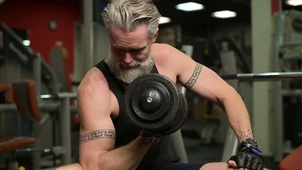 Close-up of a gray-haired bodybuilder in the gym. Gray-haired man pumping biceps