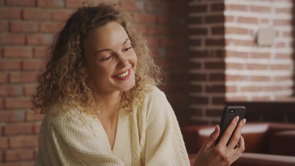 Happy Young Curly Blond Caucasian Woman Chatting on Her Smartphone Using a Video Call with Friends