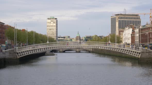 People Cross At Ha'penny Bridge Over Liffey River In Dublin, Ireland. - wide shot