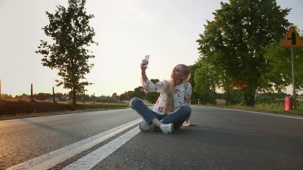 Young Woman Taking Selfie on Road. Lovely Young Lady Smiling and Posing for Selfie While Sitting on