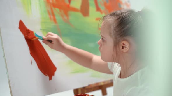 Girl with Down Syndrome Draws with a Brush on a Large Canvas in a White Room Kid Girl with Special