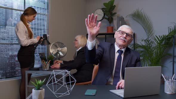 Senior Businessman with Colleagues Team Waves Palm in Hello Gesture Welcomes Someone in Office