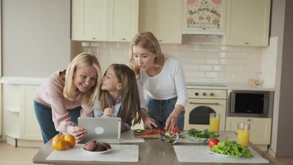 Three Female Generation are Cooking Vegetables and Watching Recipes Tablet