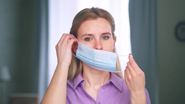 Young woman putting on a medical blue mask at home