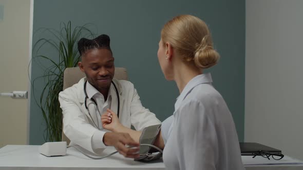 Young Male Doctor Checking Blood Pressure to Female Patient Indoors