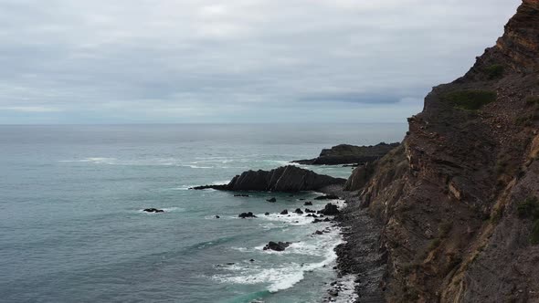 Rugged coastline of Praia da Arrifana in west Portugal on overcast day, Aerial flyover view