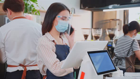 Asian cafe business owner wear face shield and mask due to Covid 19 talking to customer by phone.