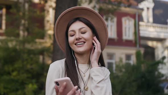 Beautiful Young Modern Woman in Lovely Hat Standing in the Mansion's Yard and Listening Music