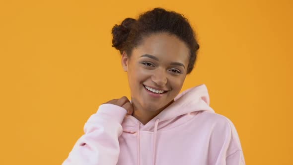 Joyful Female Teenager in Stylish Pink Hoodie Smiling Camera Yellow Background