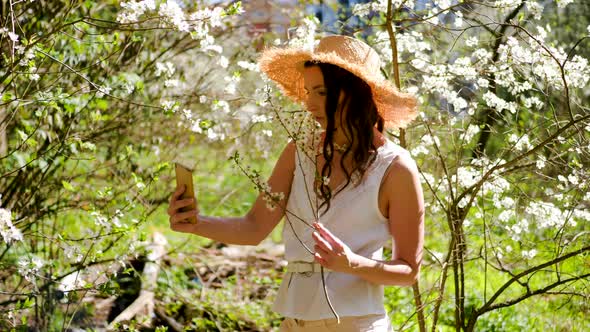 Brunette Woman with Long Hair in a Straw Hat Stands in the Apple Orchard