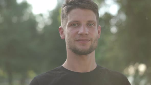 Headshot Portrait of Young Caucasian Bearded Brunette Man with Grey Eyes Posing in Sunbeam Outdoors