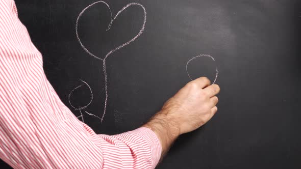 A man's hand in a red and white striped shirt draws a man with a heart on a string on the blackboard