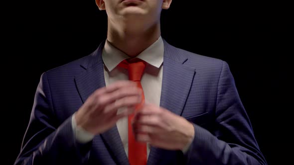 A Young Man in a Simple Blue Suit and White Shirt Neatly Straightens His Red Tie Hands