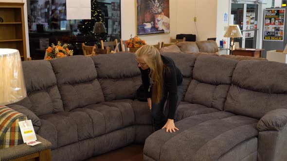 Pretty mature blonde woman getting comfortable on a couch in furniture showroom with Christmas tree