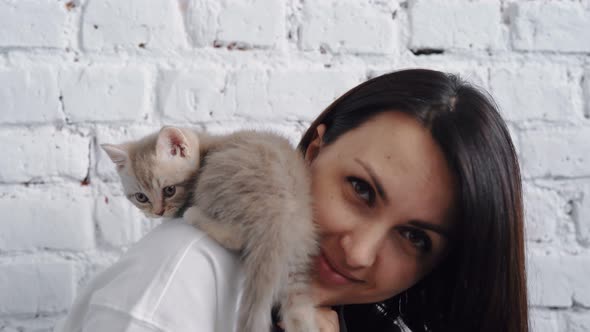 Young Beautiful Brunette White Man Holds a Gray Kitten on His Shoulders and Plays with Him on a