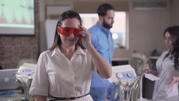 Young Beautiful Female Dentist Putting on Protective Eyeglasses and Turning on Curing Lights As Her