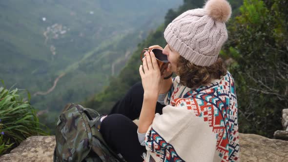 Hiker Woman In Poncho Drinks Tea Camping In Mountains