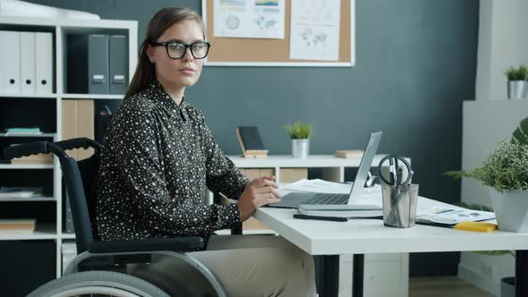 Slow Motion of Attractive Young Businesswoman in Wheelchair Looking at Camera at Work